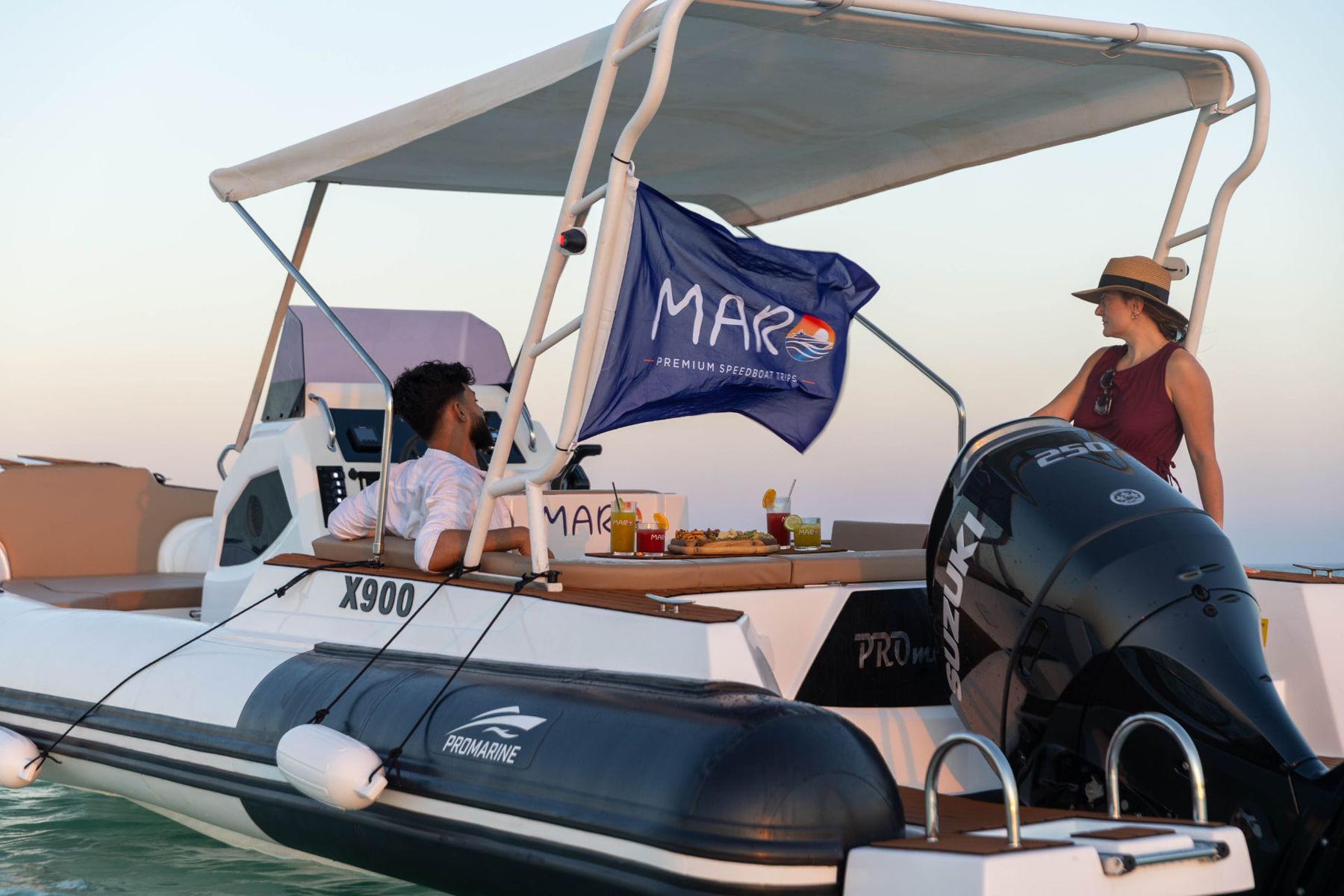 Guests sharing drinks on board at sunset with the Maro Redsea flag against a golden Red Sea sky