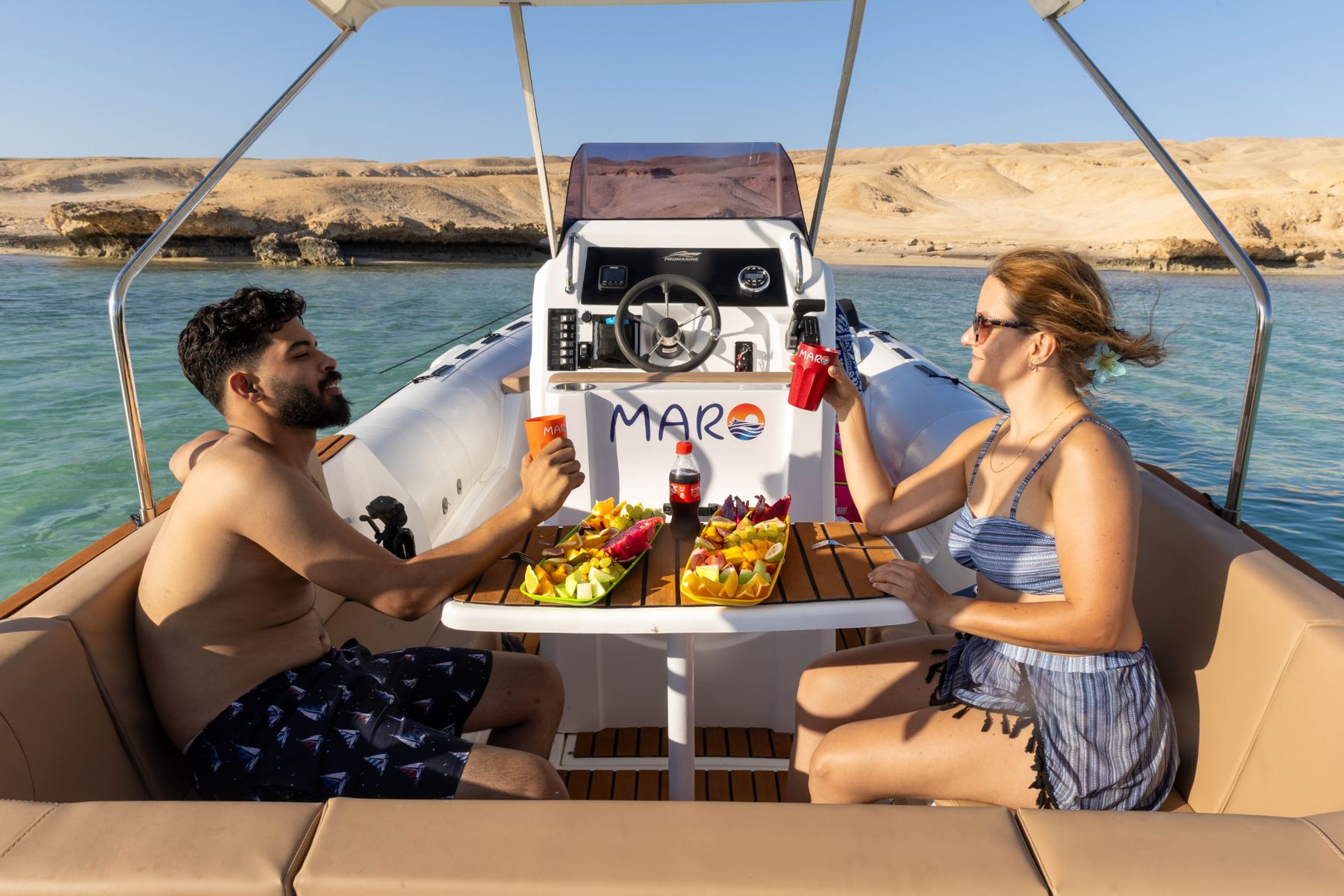 Two guests enjoying fresh fruit and cold drinks at the onboard table of the Maro Redsea speedboat