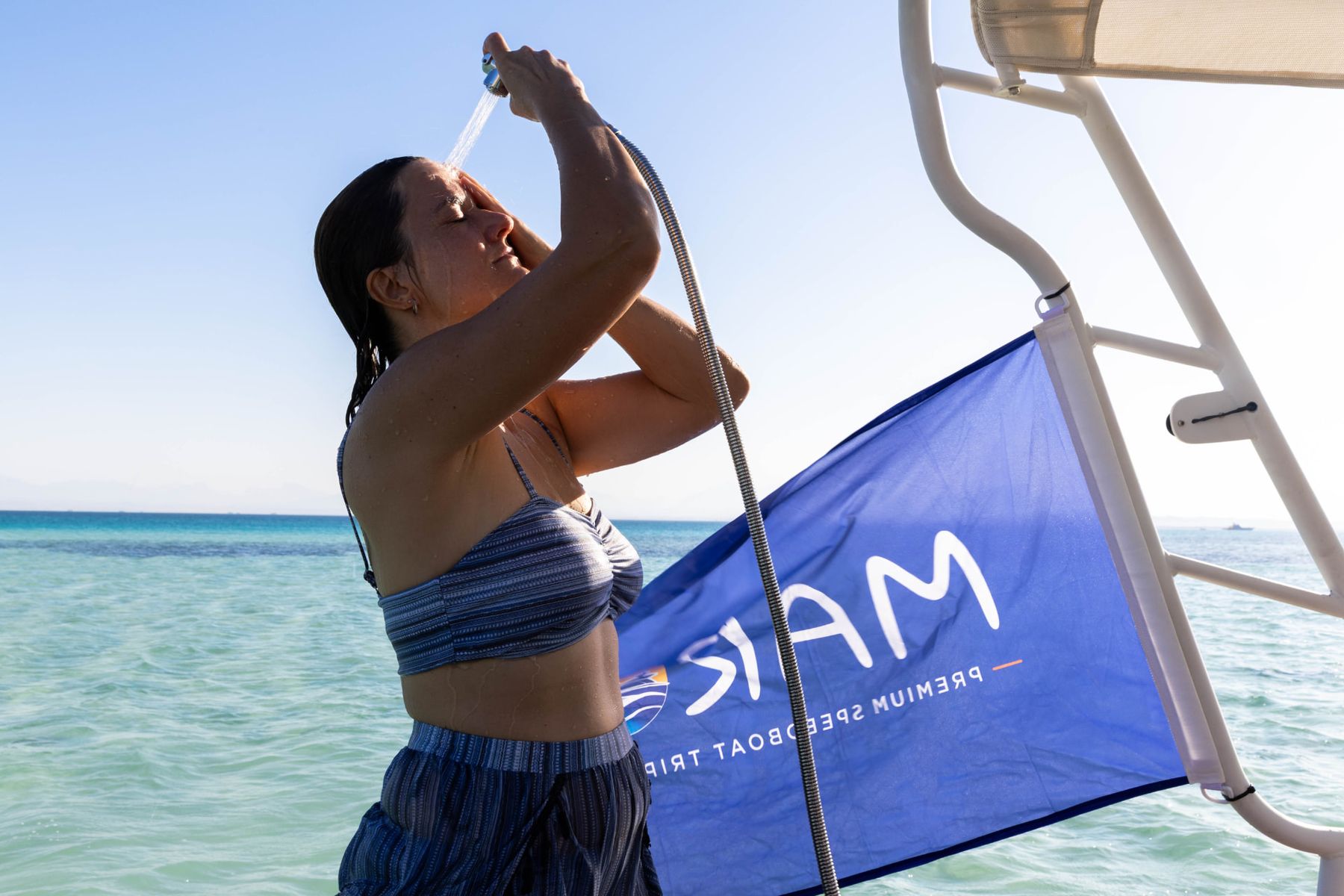 Guest rinsing off with the onboard freshwater shower beside the Maro Redsea flag