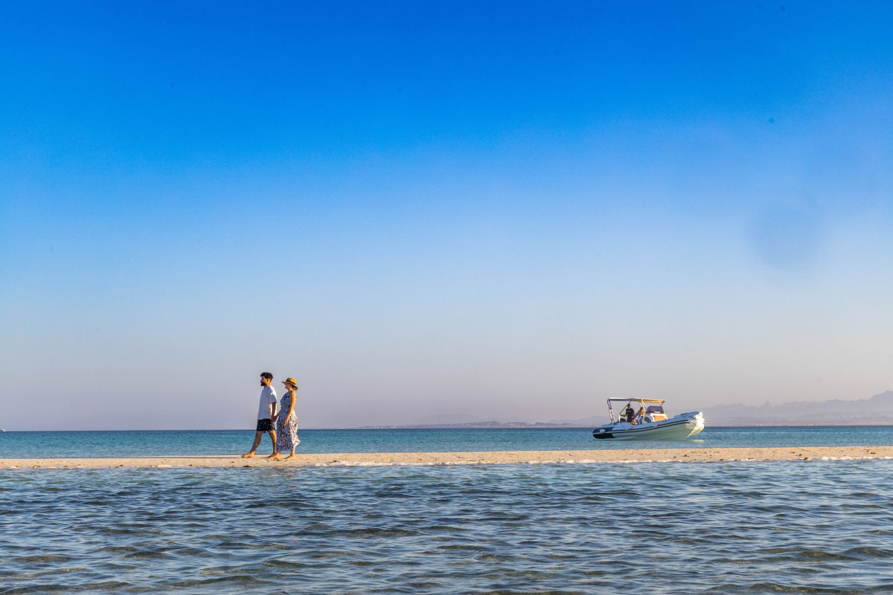 A couple walking along a quiet Red Sea sandbank with the Maro Redsea speedboat waiting nearby