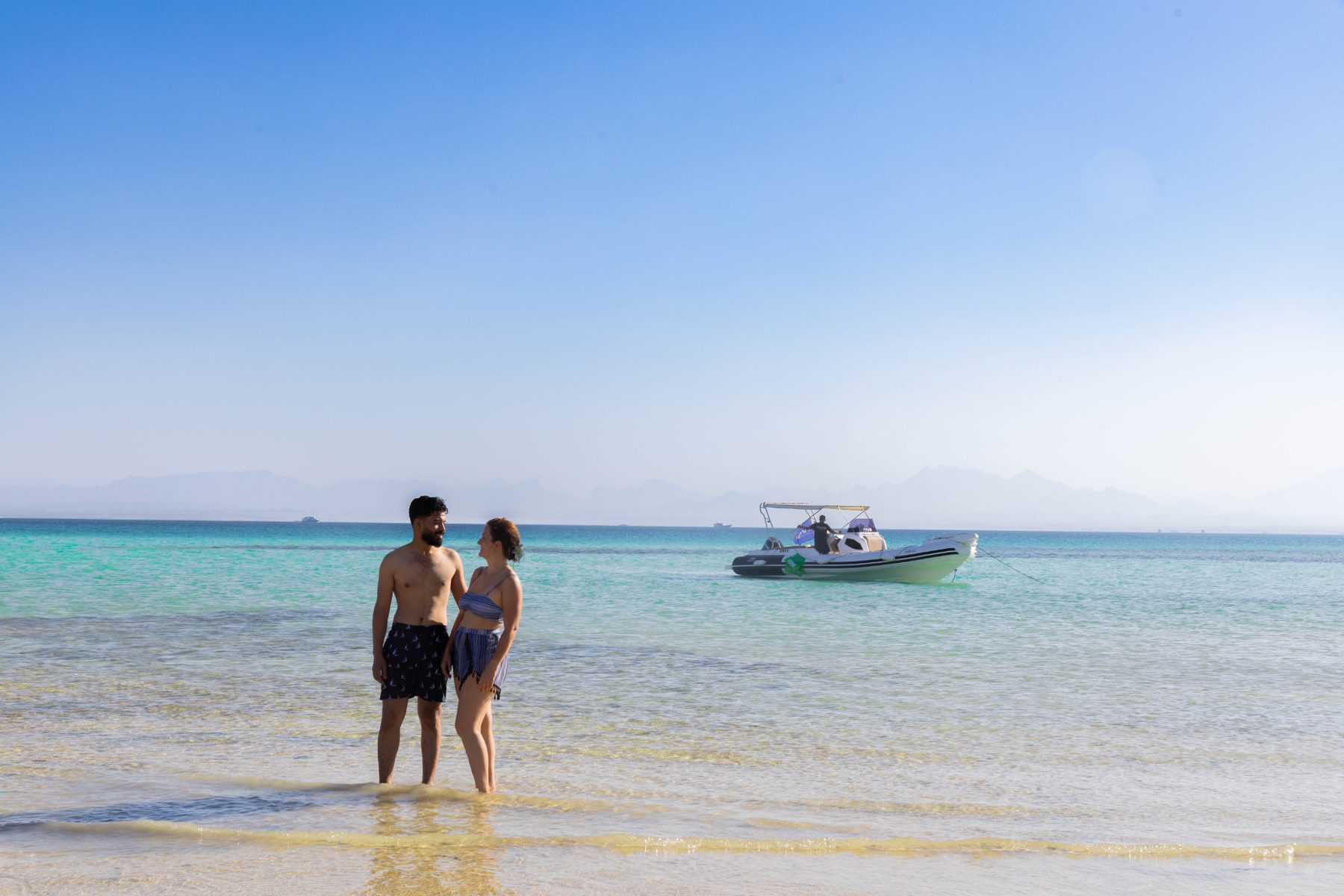 A couple standing in the shallow turquoise water with the Maro Redsea speedboat anchored behind them